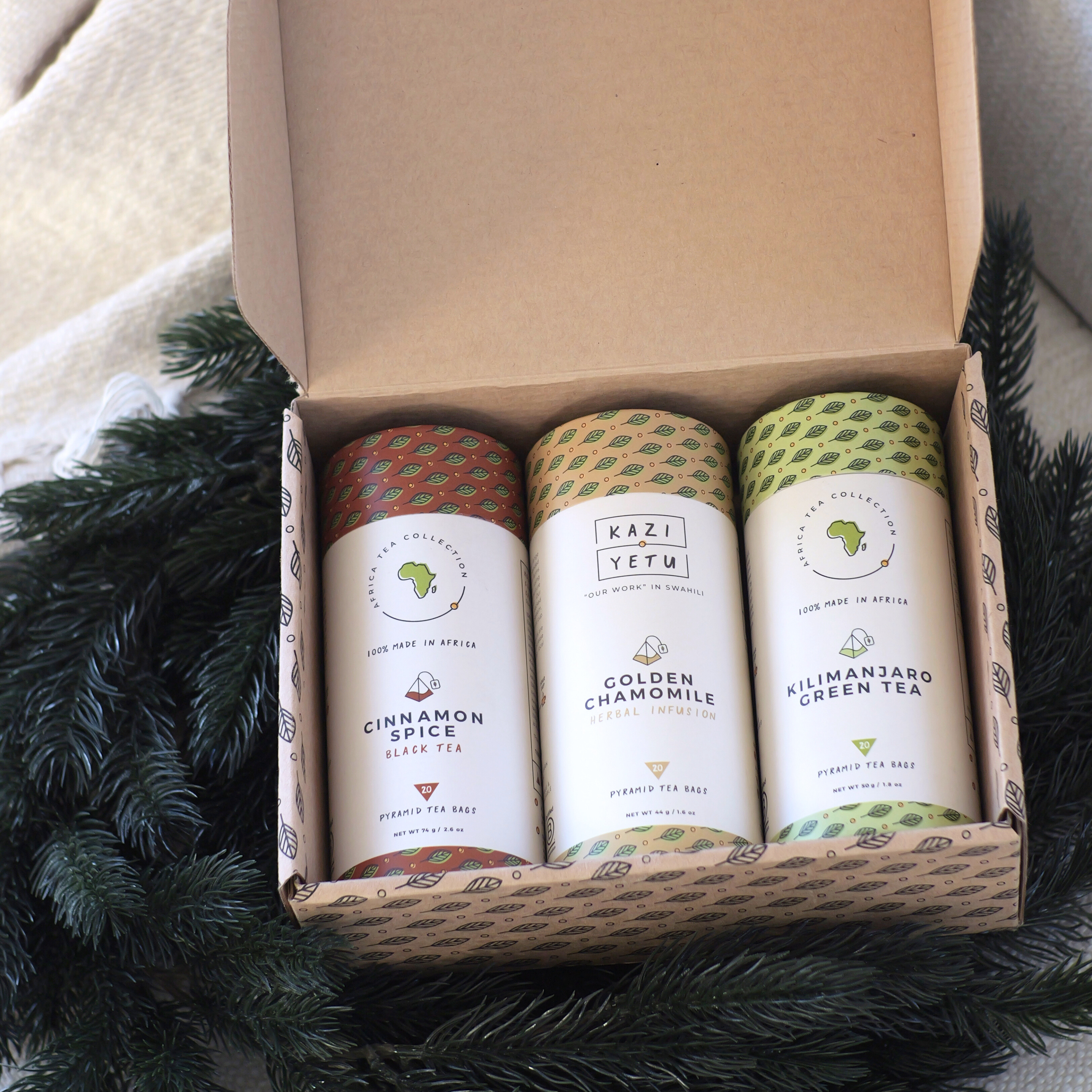 Three tea blends in a cardboard box with 'Kazi Yetu' branding on a textured surface.