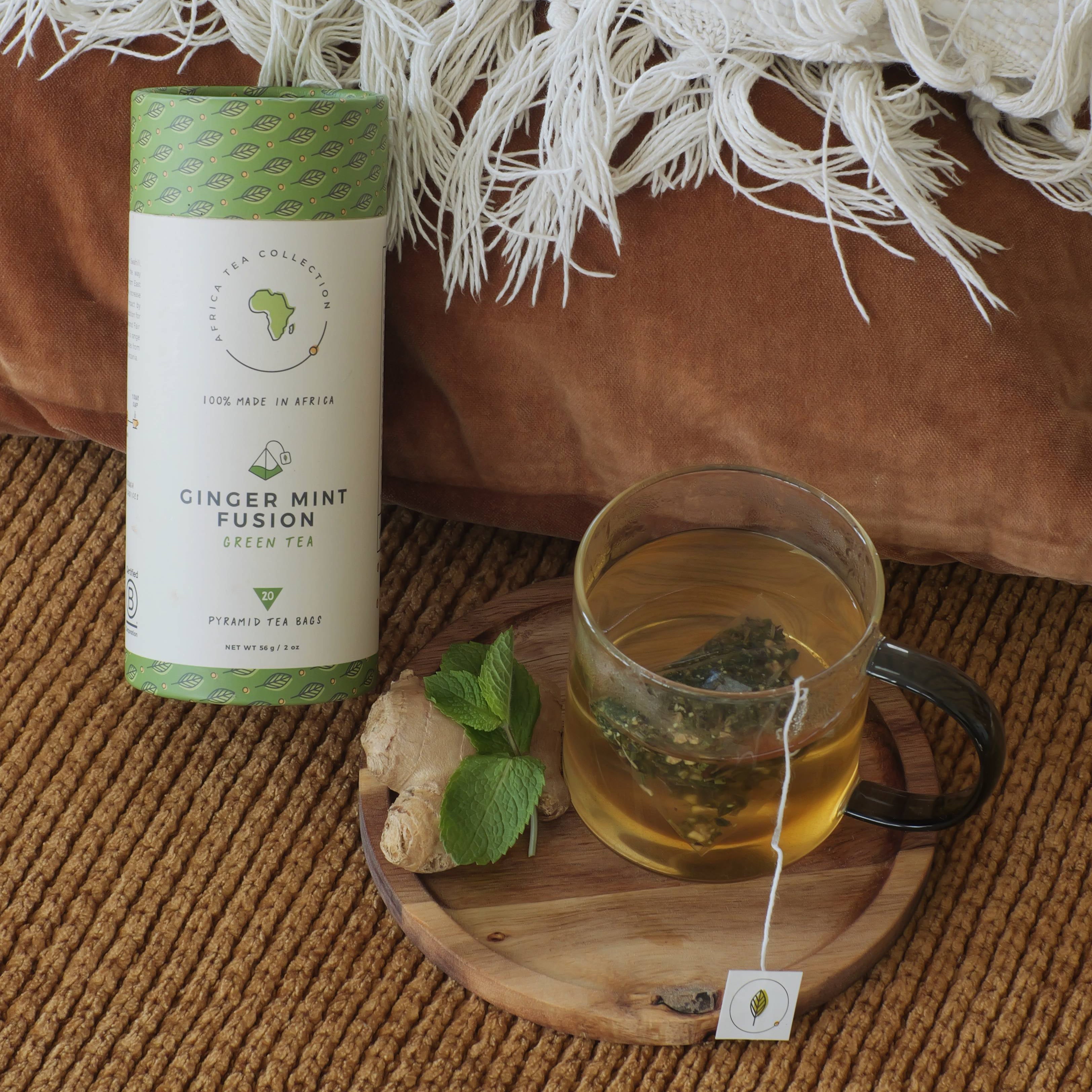 Ginger Mint Fusion tea blend with a glass of tea on a wooden coaster, surrounded by a white blanket and brown cushion.