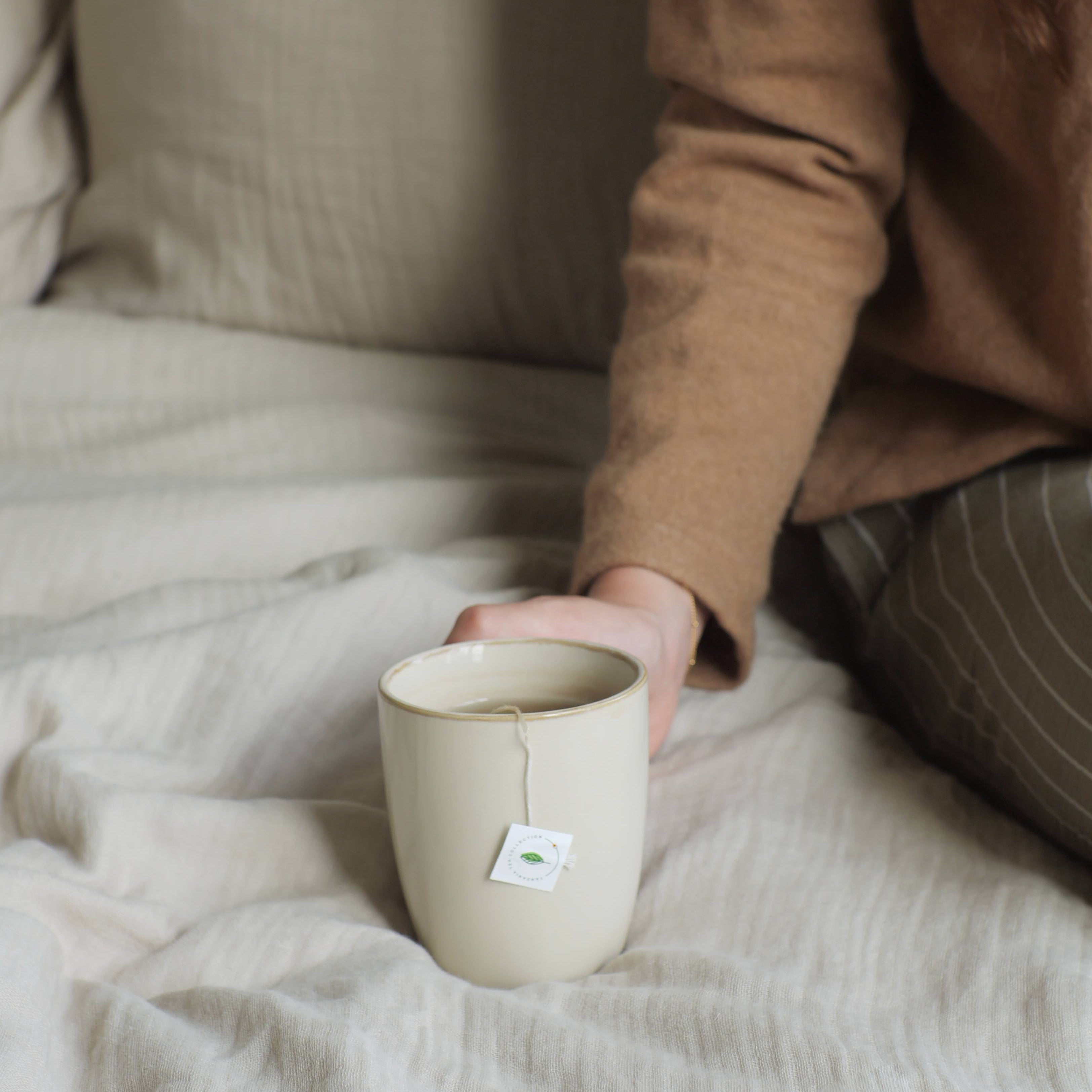 Person holding a mug on a bed with neutral tones