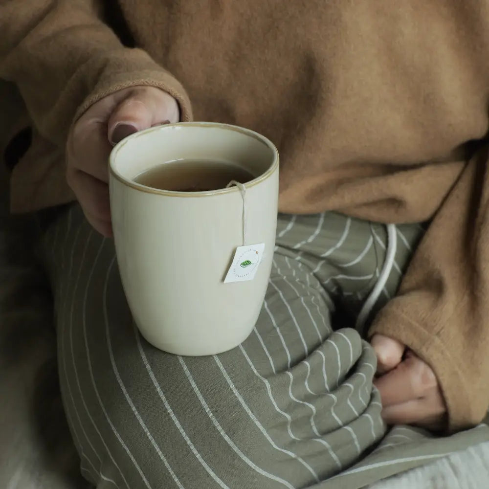 Person holding a white mug with a green label on a striped cushion